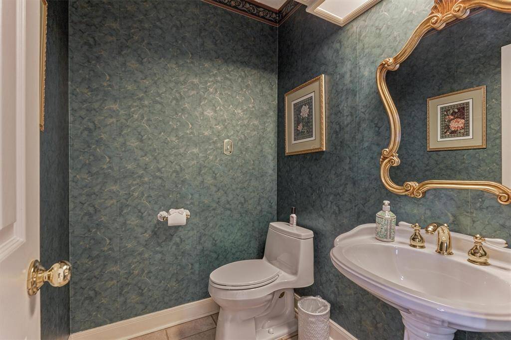 Elegant powder room with pedestal sink, gold accents, and rich wall treatment—conveniently located for guests near the main living area.