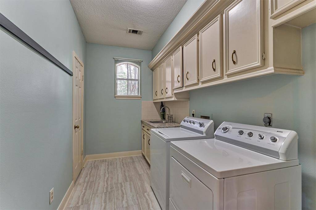 Spacious laundry room with built-in cabinetry, granite counter, deep sink, and tile flooring—conveniently located next to the porte-cochère entry and across from the guest half bath.