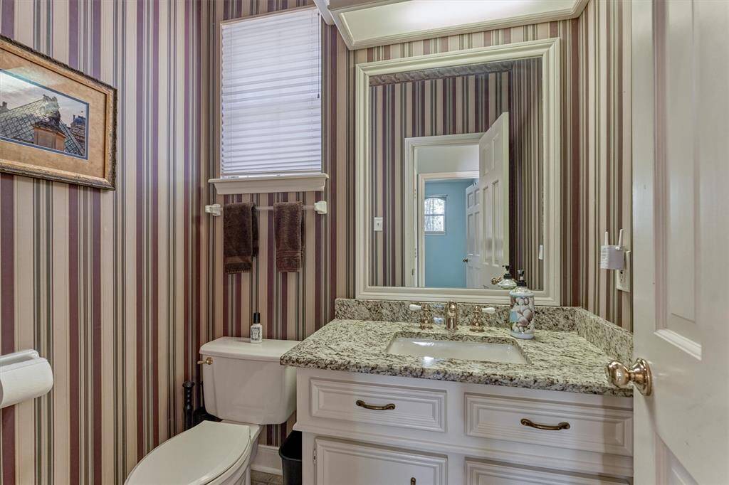 Stylish half bath with granite vanity and classic striped wallpaper—perfectly positioned between the porte-cochère entrance and the poolside patio for easy guest access.