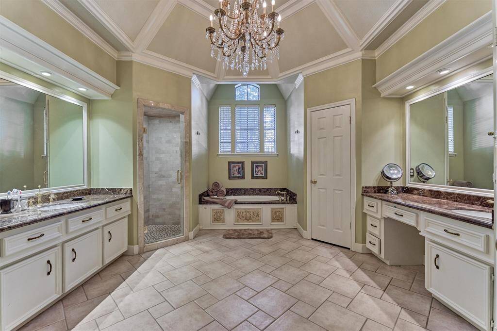 Retreat-style en-suite with soaring vaulted ceilings, luxurious chandelier, oversized walk-in shower, and a deep soaking tub framed by decorative panels and natural light.