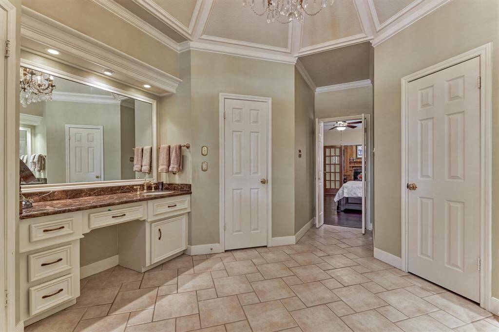 Expansive primary bathroom featuring elegant tile flooring, dual vanities, and custom cabinetry—complete with separate his and hers closets for ultimate organization.