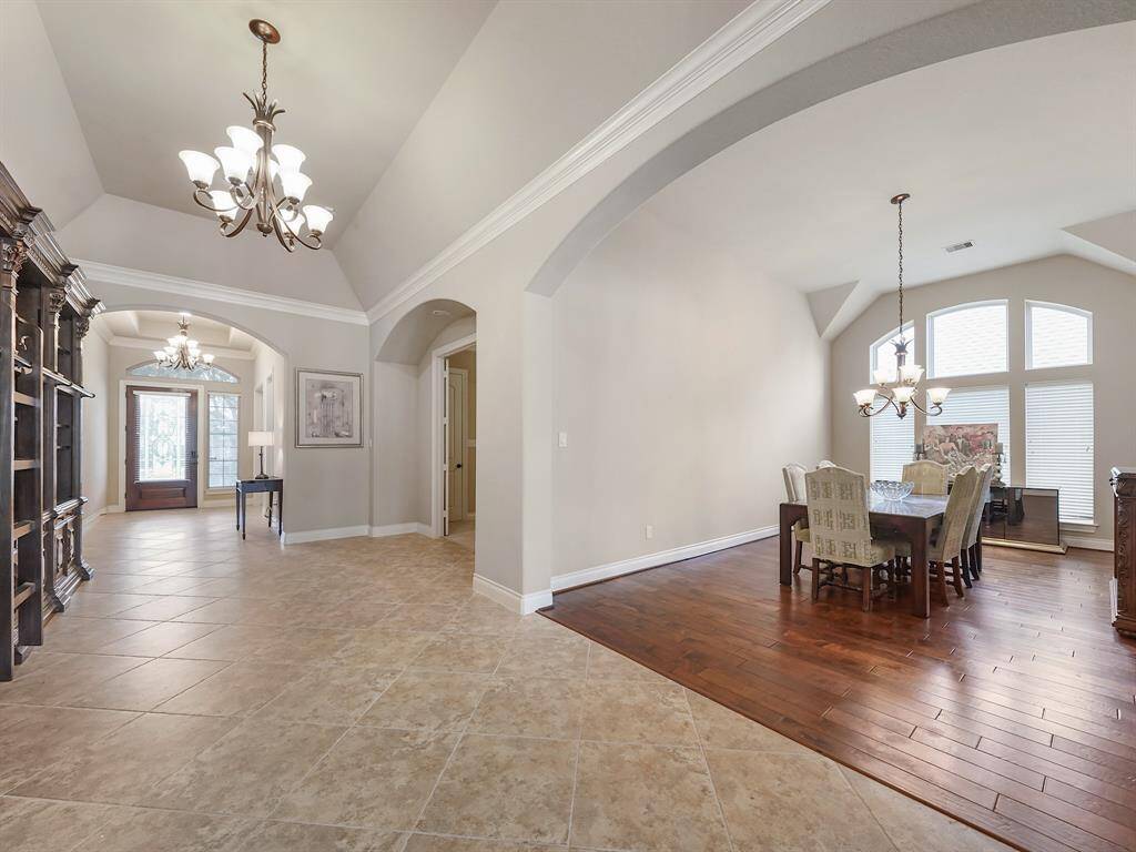This exquisite home boasts a breathtaking entry featuring intricate crown molding, a soaring vaulted ceiling, and elegant chandeliers that cast a warm, inviting glow. The formal dining room is a masterpiece, showcasing rich wood floors, grand arched windows that flood the space with natural light, and an arched entryway that adds a touch of timeless sophistication.