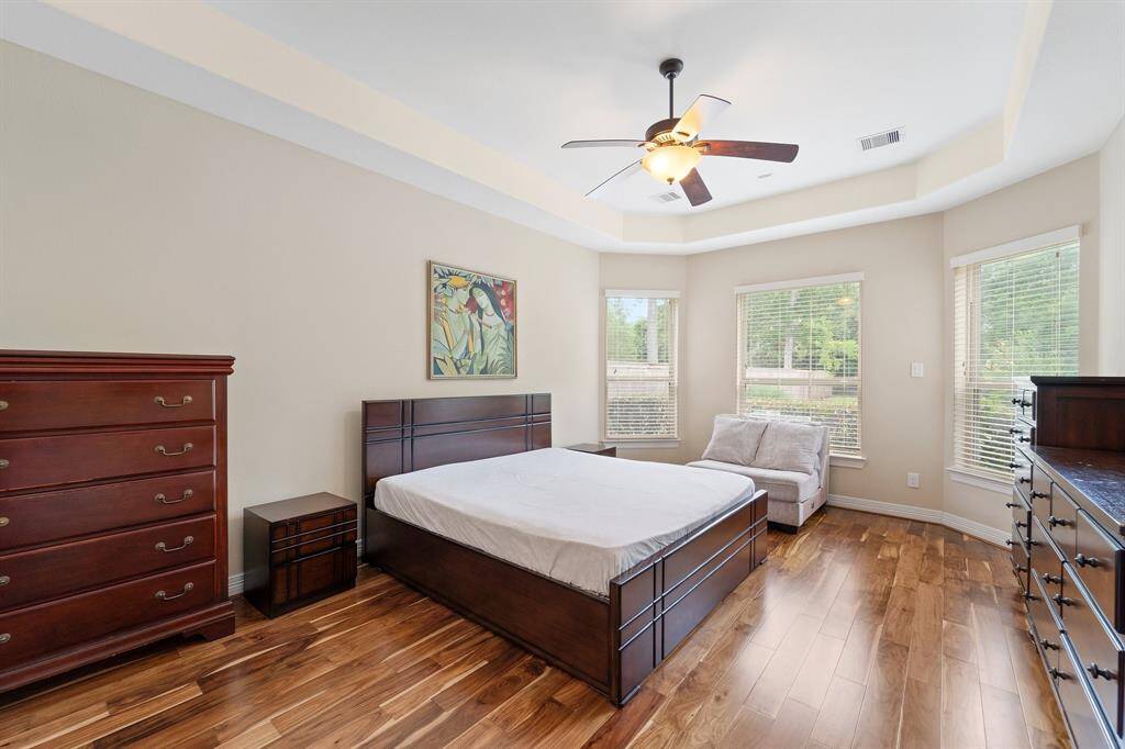 Elegant primary suite with tray ceiling, rich hardwood floors, and a wall of windows overlooking the backyard.