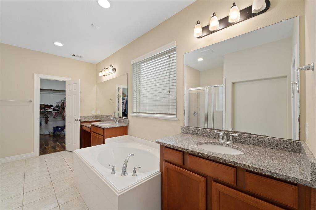 Spacious primary bath features dual granite vanities, a large soaking tub, and direct access to an expansive walk-in closet.