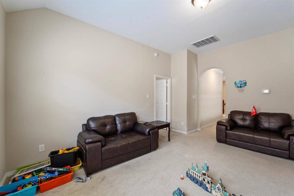 Expansive upstairs game room with ample space for lounging and play, featuring multiple seating areas and an arched hallway entry.