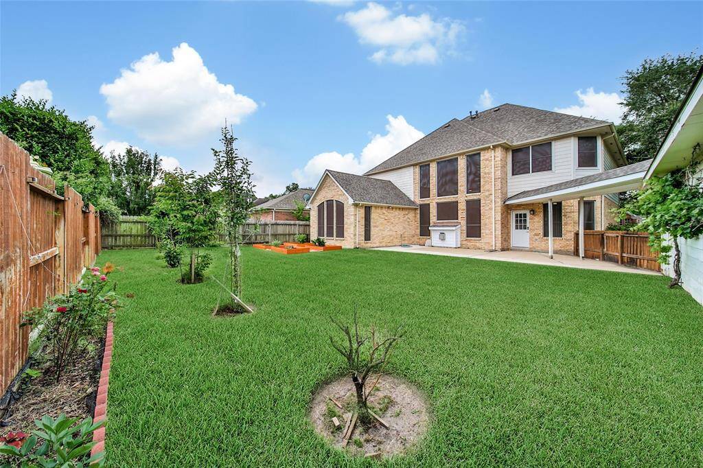 A verdant yard boasts lush grass and a variety of fruit plants and raised garden beds for your enjoyment.