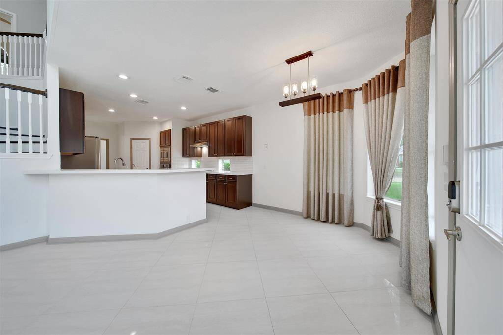 The kitchen opens to the breakfast room and living room via a long seating bar. The breakfast room features custom drapes and a charming chandelier.