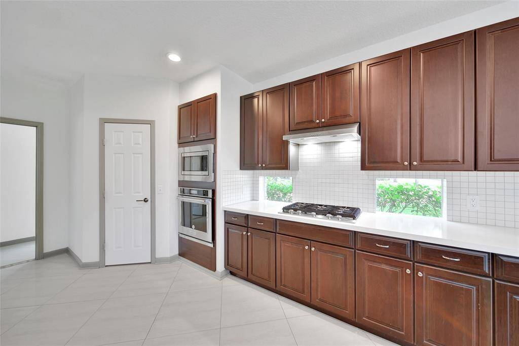 Side windows flank the five burner gas cooktop, letting natural light flow through the workspace so you can enjoy nature even when you're cooking. A built-in wall oven and microwave are at the end of the kitchen, with a walk-in pantry for storage, and the utility room to the left.
