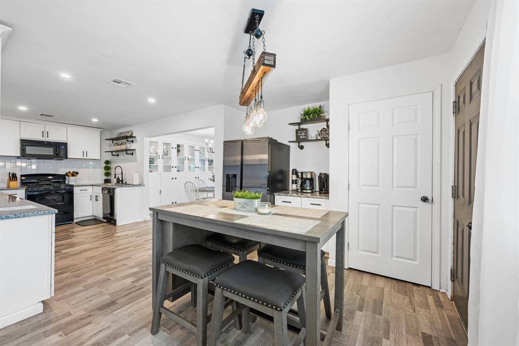 Modern kitchen with open layout, featuring white cabinets, stainless steel appliances, and a stylish island with seating. The space is bright and inviting, with wood-look flooring and contemporary lighting.