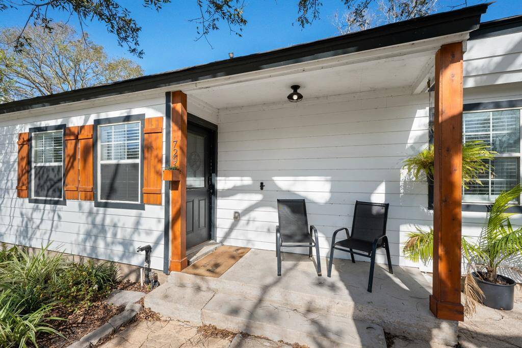 Charming front porch with warm wooden accents, perfect for relaxing. The house features white hardy plank siding, updated windows with shutters, and inviting landscaping.