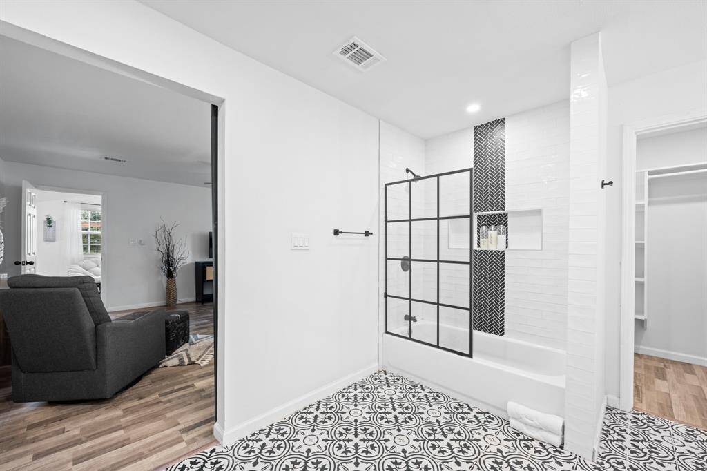 This photo showcases a modern bathroom with a stylish black and white motif. It features a bathtub with a glass door and decorative tile work. The room connects to the bedroom with wood-look flooring and a cozy atmosphere.