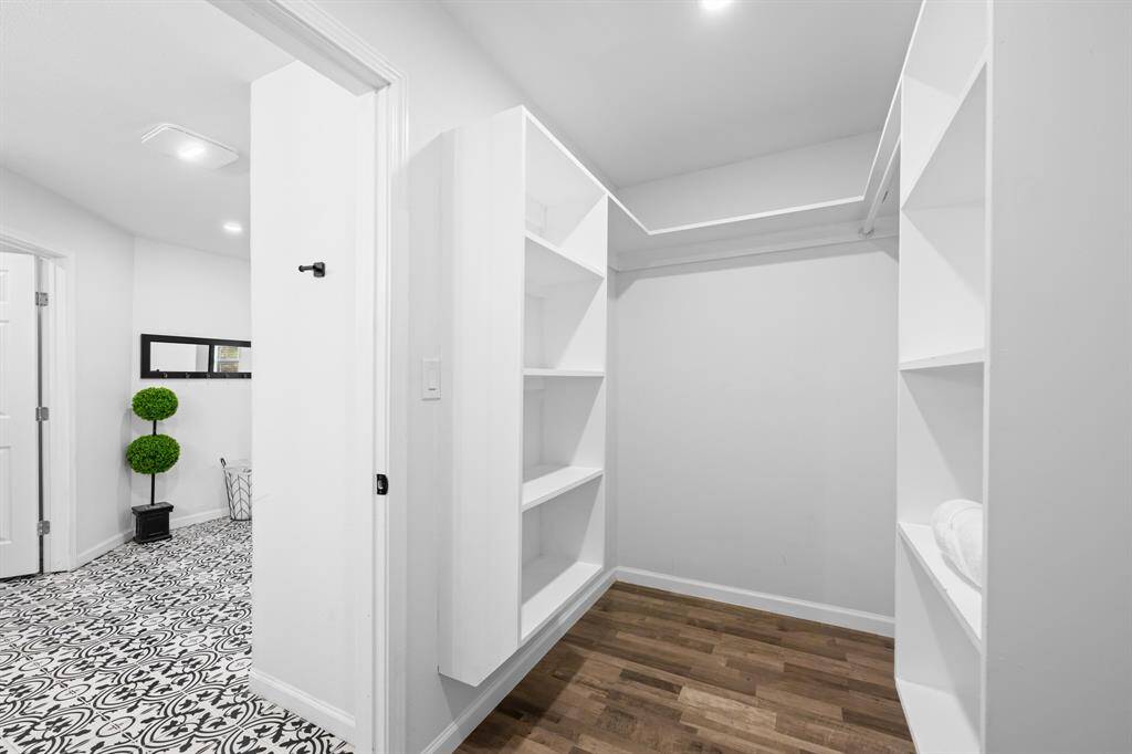 This photo showcases a spacious walk-in closet with white shelving and hanging space. It opens to a stylish area with patterned tile flooring and a decorative plant, providing a sleek and organized look.