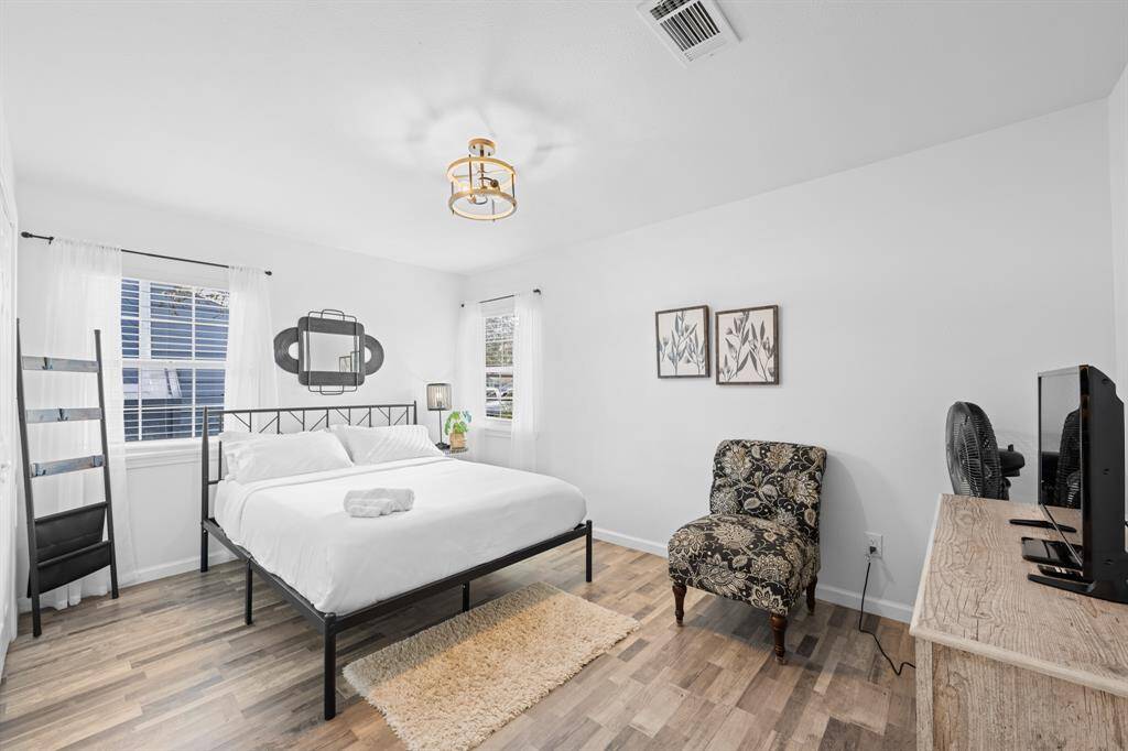 Bright and airy bedroom with modern decor, featuring a comfortable bed, large windows with ample natural light, a patterned chair, and a wooden dresser.