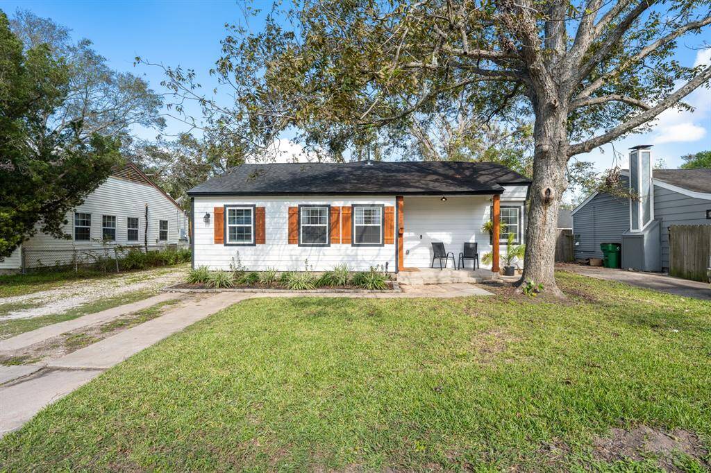 Charming single-story home with a cozy front porch, nestled under a large tree. It features a neat lawn and a driveway, offering a welcoming and serene atmosphere.