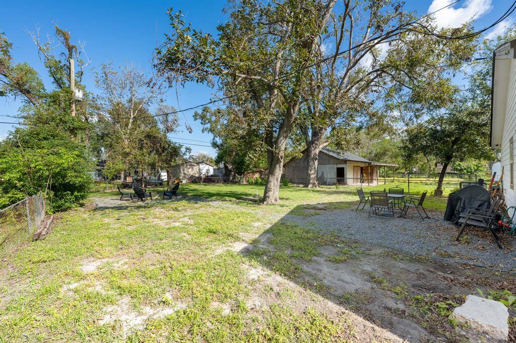 Spacious backyard with mature trees, a gravel patio area featuring outdoor seating, offering a mix of greenery and functional outdoor space.