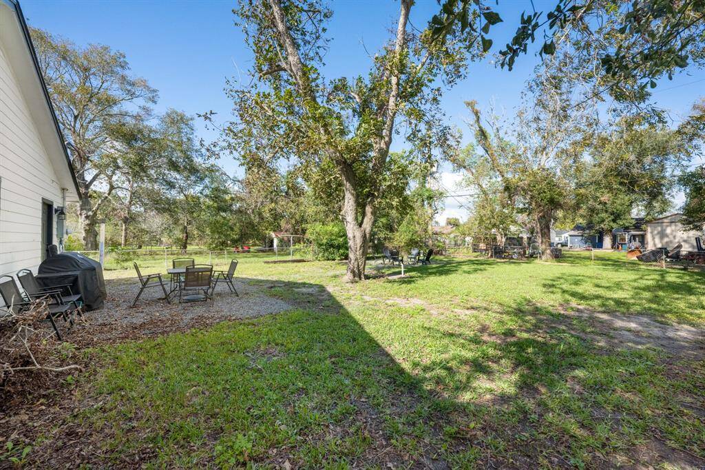 The photo showcases a spacious backyard with mature trees providing shade. There's a patio area with outdoor seating and a grill, offering a comfortable space for relaxation or entertaining. The yard is grassy and well-maintained, ideal for family activities or gardening.