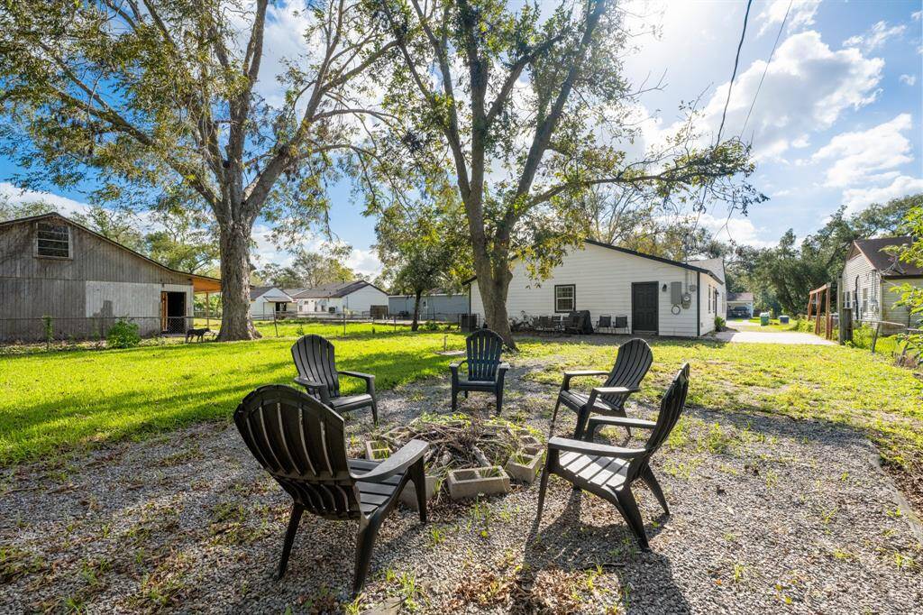 Spacious backyard featuring a cozy fire pit area with Adirondack chairs, mature trees providing shade, and a view of the house. Ideal for outdoor gatherings and relaxation.