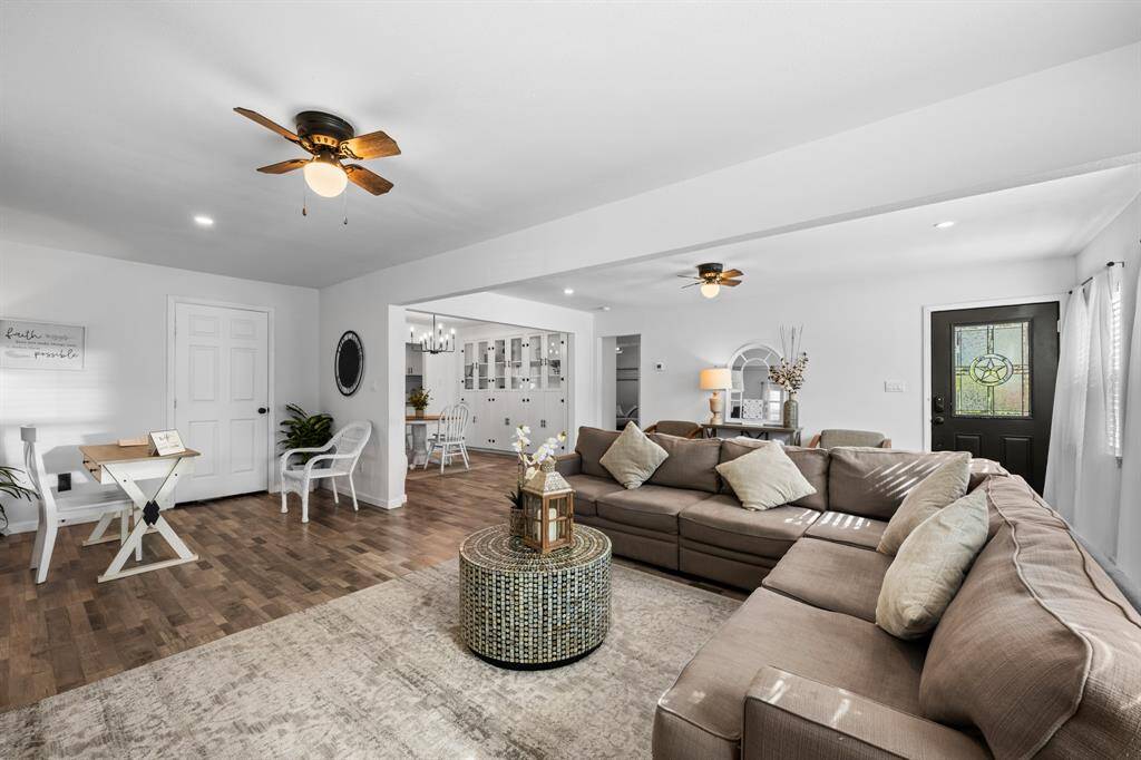 This photo showcases a spacious, open-concept living area with abundant natural light, featuring a large sectional sofa, wood-look flooring, and a cozy dining nook. The room is bright and inviting, with ceiling fans and a modern design.