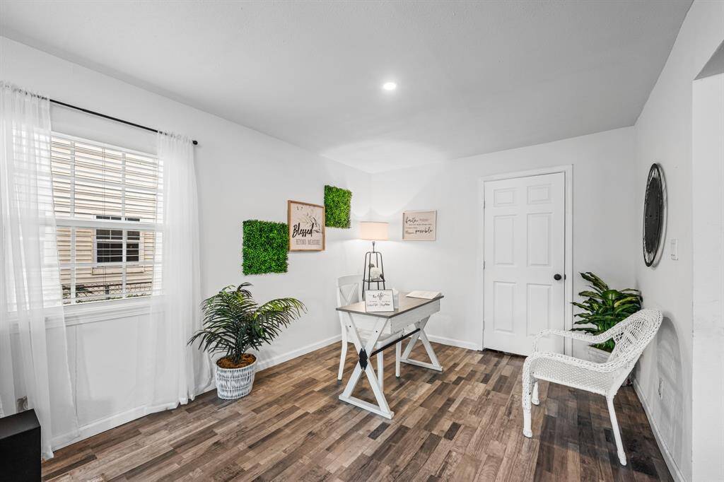 This office space is bright and inviting, featuring a modern desk, hardwood floors, and plenty of natural light. It's decorated with a greenery and wall art backdrop, making it perfect for a home office or study.