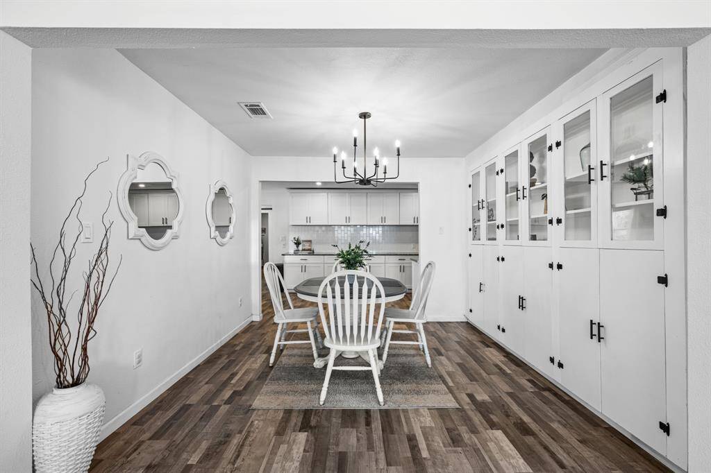 This dining area features a modern chandelier, built-in cabinets for ample storage, and a cozy table setup. The space is bright with white walls and wood-look vinyl plank flooring, seamlessly connecting to the kitchen.
