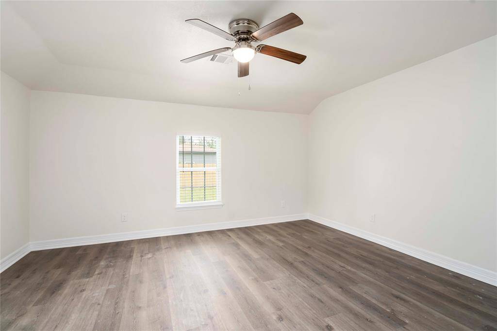This room features light-colored walls, wood-style flooring, a ceiling fan, and a single window, offering a bright and airy atmosphere.