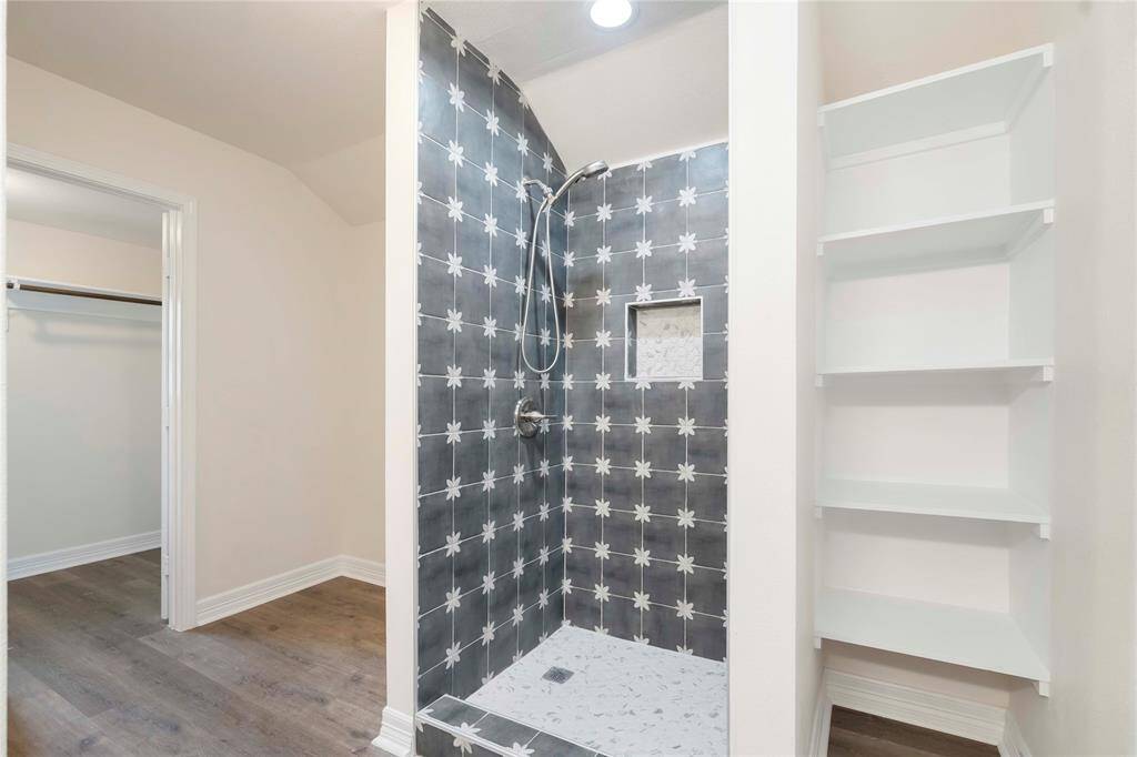 Elegant primary suite shower with stylish tile design and convenient built-in shelving.