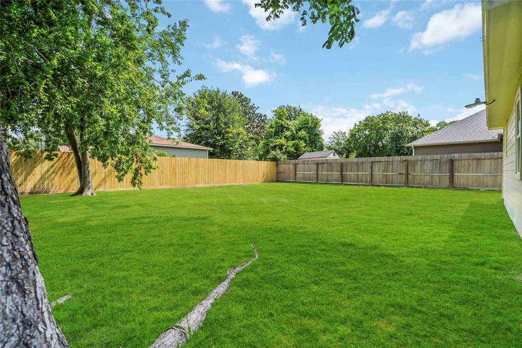 This photo showcases a spacious, well-maintained backyard with lush green grass, surrounded by a wooden fence for privacy. The area is bordered by trees, providing a serene and natural setting, ideal for outdoor activities or relaxation.