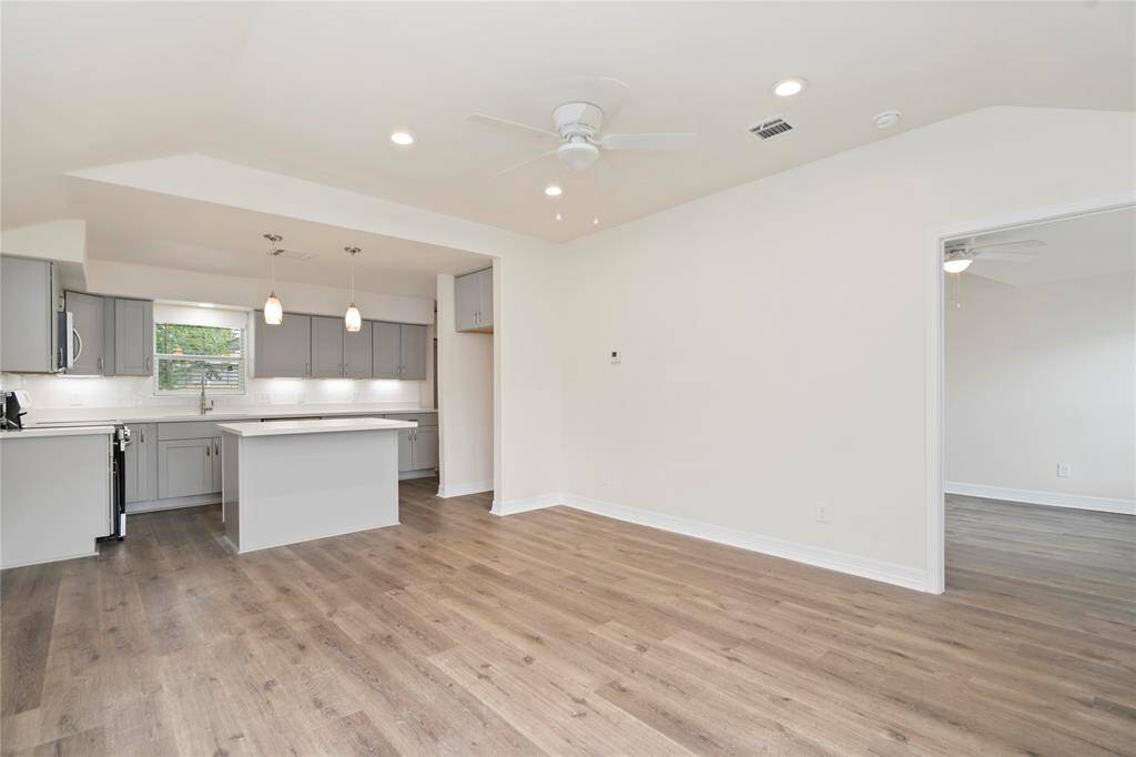 This photo showcases a bright, open-concept living space with a modern kitchen featuring gray cabinets, a central island, and pendant lighting. The room has wood flooring, recessed lighting, and neutral walls, creating a welcoming atmosphere.