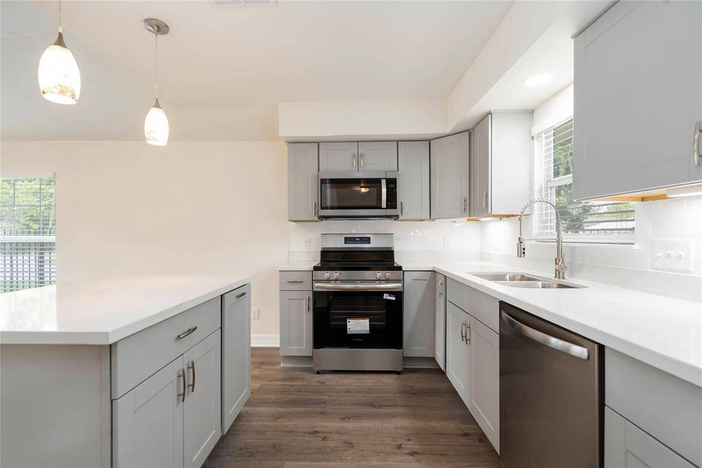 This modern kitchen features sleek gray cabinets, stainless steel appliances, and a bright, open layout with ample counter space. The hardwood floors and pendant lighting add a touch of elegance.