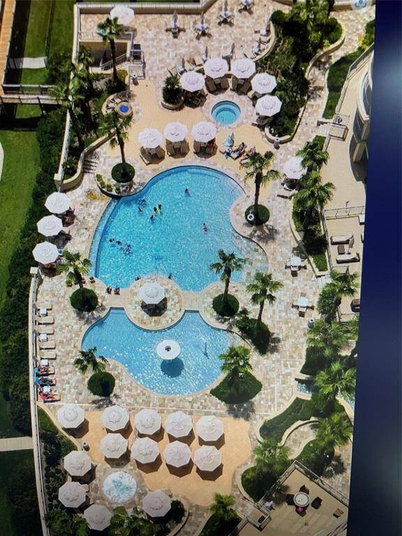 Expansive pool deck with two pools, two hot tubs, and a fire pit, offering ample seating and stunning ocean views.