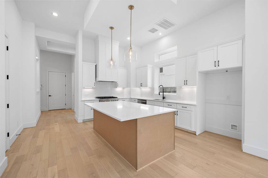 Alternate view of spacious island with beautiful quartz countertops and stainless appliances. Large walk-in storage closet and pantry are located on the left. (Photo is of a previously completed home.)