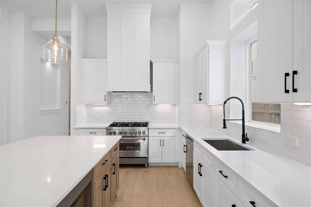 Closeup of large island kitchen with 6-burner stove, under cabinet lighting, soft-close drawers, and black matte hardware. (Photo is of a previously completed home.)