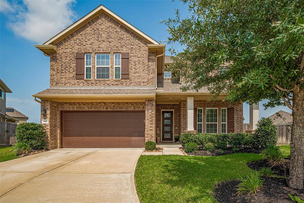 A charming two-story brick home with a gable roof and a two-car garage. The well-maintained front yard features a lush lawn, manicured shrubs, and a mature tree, enhancing the home's curb appeal. A covered entryway leads to the front door, providing a welcoming entrance.