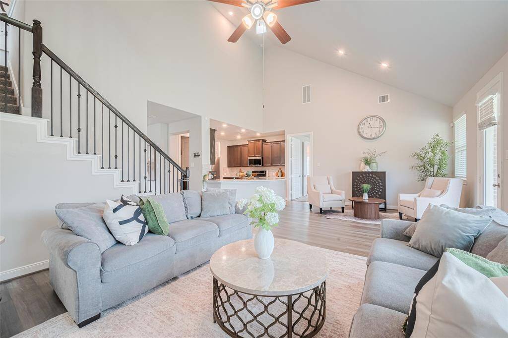This inviting living room features high ceilings, abundant natural light, and an open layout. A modern kitchen with dark cabinetry is visible in the background, enhancing the home's open concept appeal.