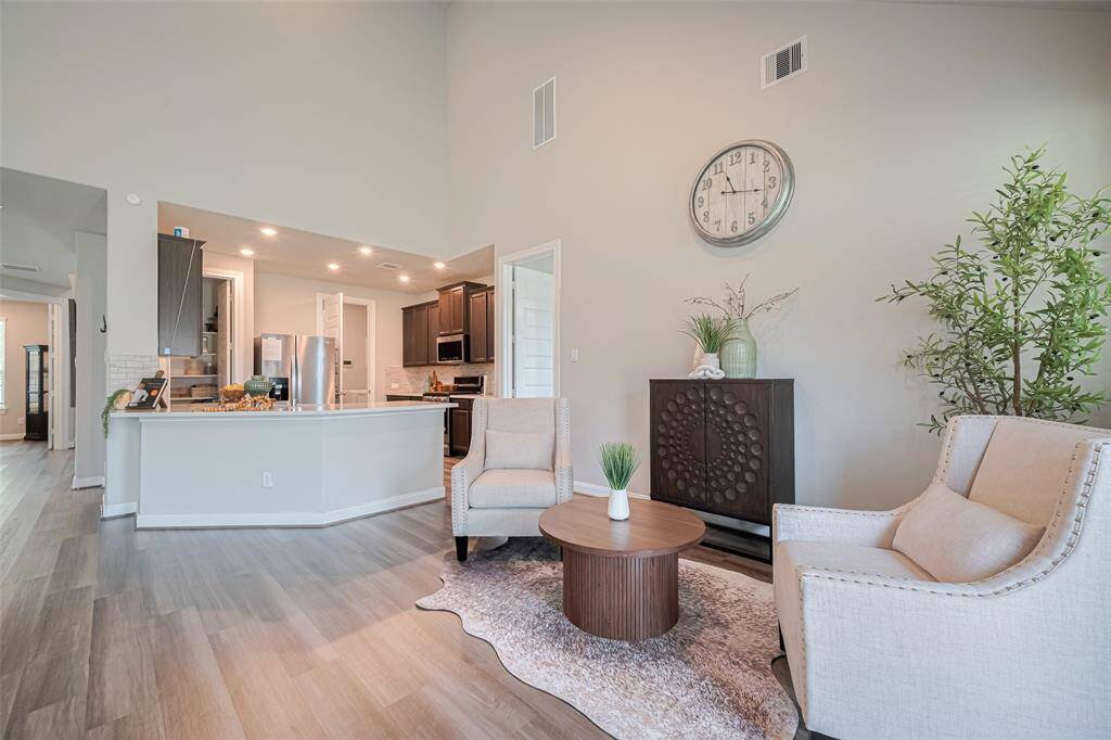 This photo showcases a bright, open-plan living space with high ceilings, featuring a modern kitchen with dark cabinets and stainless steel appliances and kitchen island