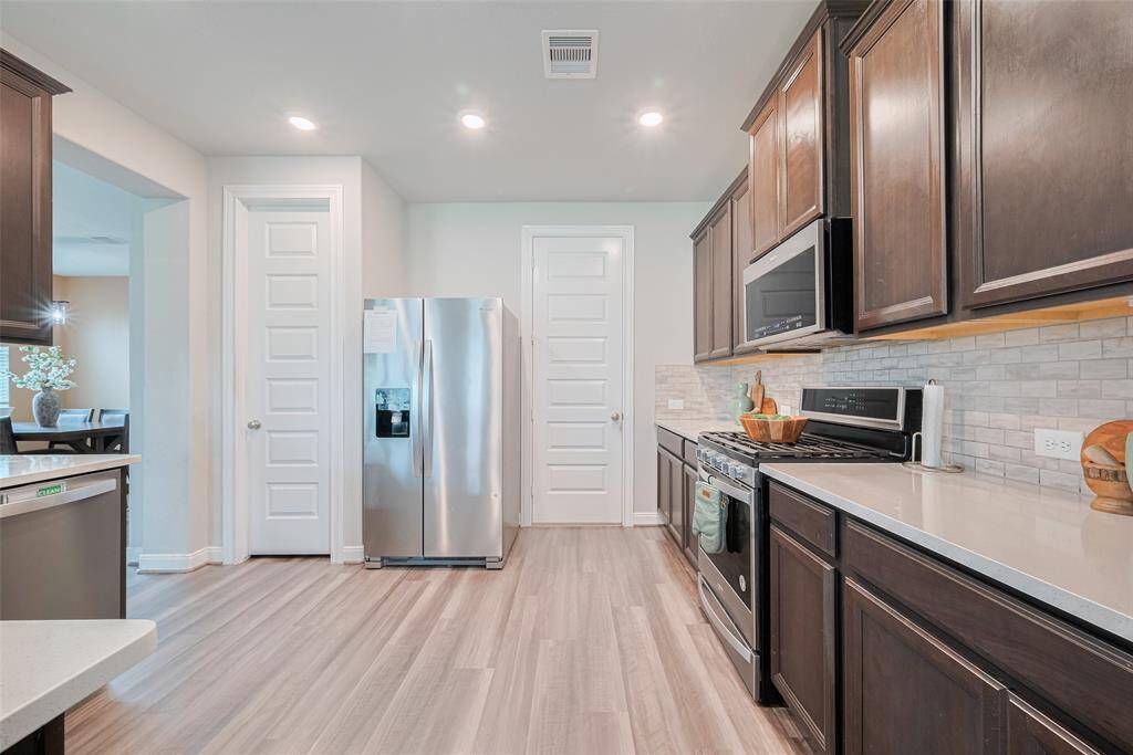 Modern kitchen with sleek stainless steel appliances, dark cabinets, and light countertops. The space features a stylish tile backsplash and wood-style flooring, creating a warm and inviting atmosphere.