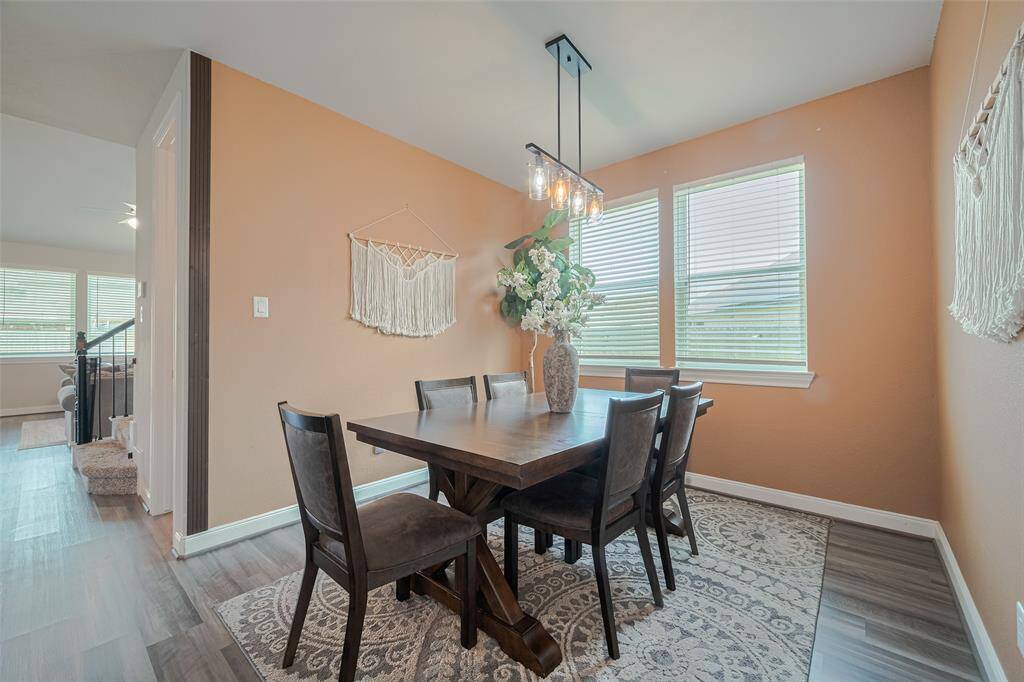 This dining area features warm peach walls, a modern light fixture, and large windows for natural light creating a cozy and inviting atmosphere.