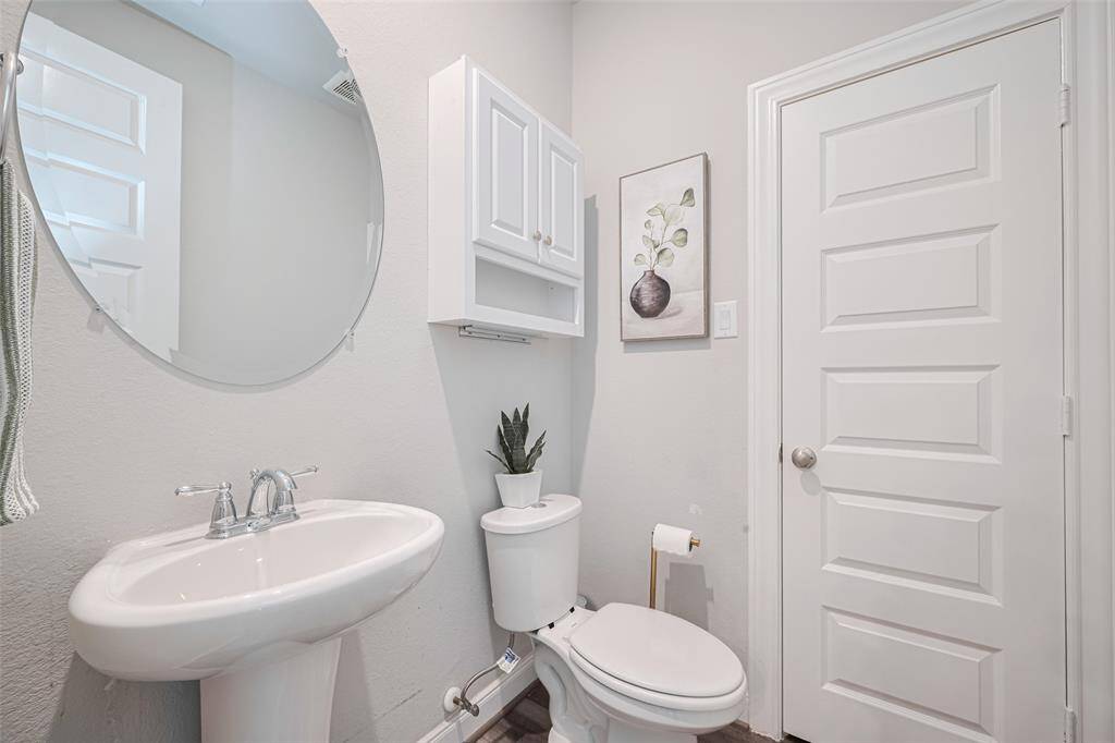 This is a compact, modern bathroom featuring a pedestal sink, a round mirror, a toilet and a closet for extra storage.