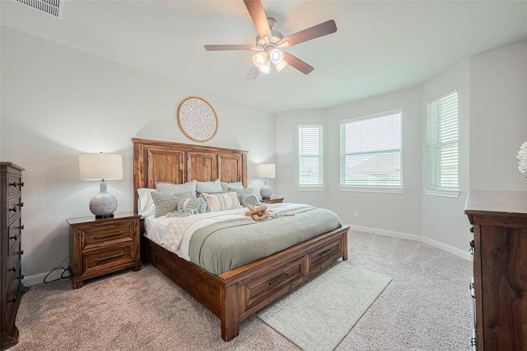 This bedroom features a spacious layout with large windows for ample natural light and a ceiling fan for comfort. Neutral walls and carpeting create a warm, inviting atmosphere.