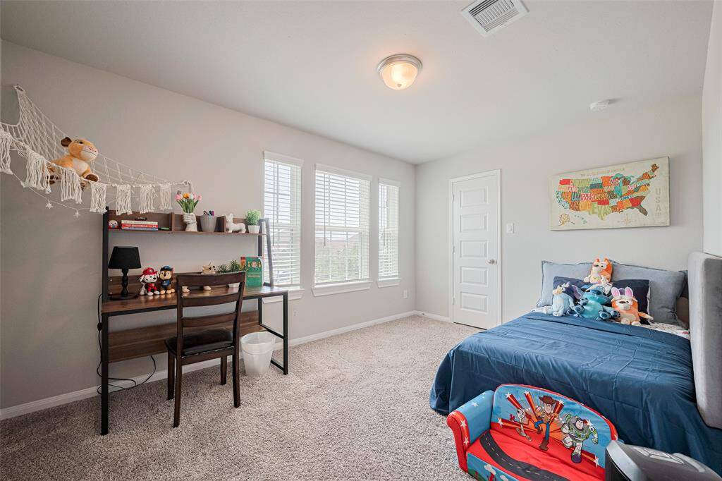 This bedroom is bright and cozy, featuring a large window, plush carpet, and neutral walls.