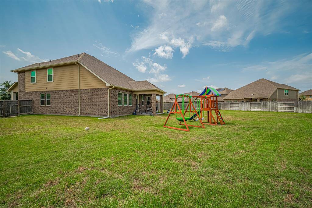 A spacious backyard with well-maintained grass, featuring a colorful play set. The house has a brick exterior and a fenced perimeter, offering privacy and a safe play area.