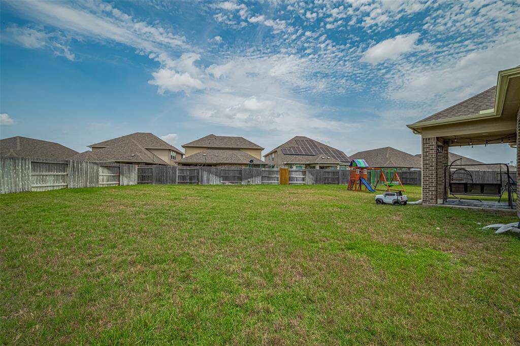 Spacious fenced backyard with a playset, patio area, and ample grass for activities, perfect for families.