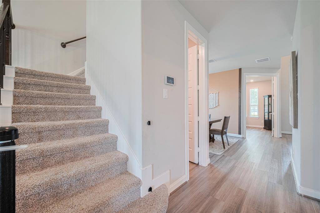 This photo showcases a bright, inviting hallway with a carpeted staircase leading to the upper floor. The hallway features wood-style flooring and leads to multiple rooms, offering a glimpse of a cozy, well-lit space with plenty of natural light.