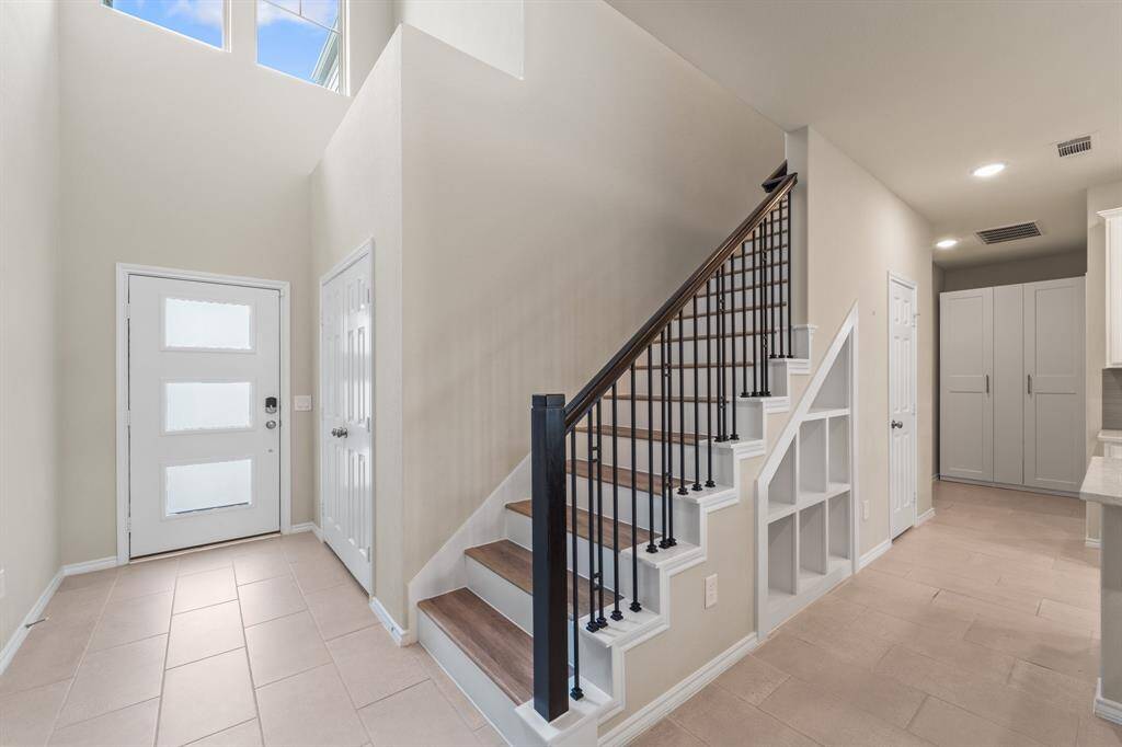 Bright and airy two-story foyer with natural light pouring in through upper windows and a modern glass-paneled front door. Clean nightlines lead to the staircase, garage hallway and laundry room access.