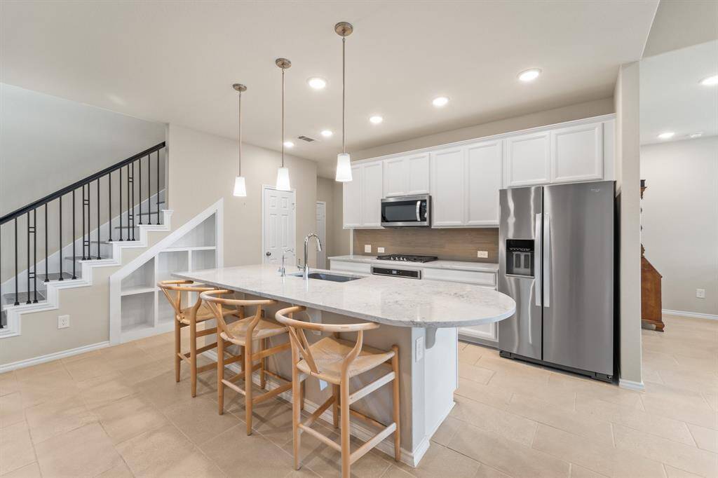 Quartz countertops, glass tile backsplash, and stainless steel appliances elevate this open kitchen, centered around a curved island with seating and upgraded pendant lighting.