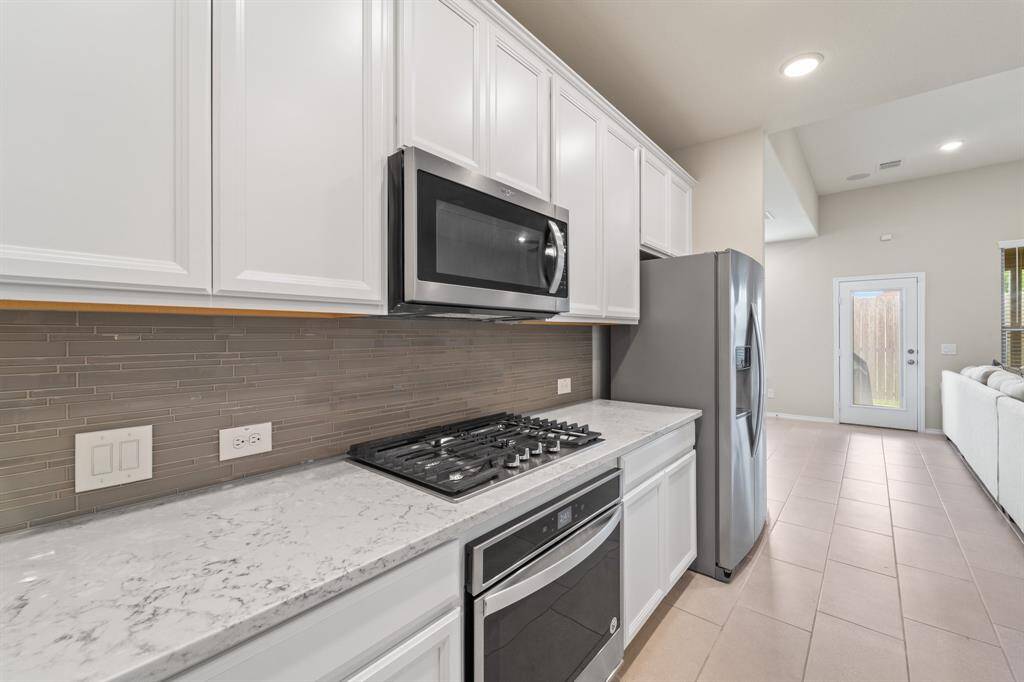 Cook like a pro with a stainless steel appliance package featuring a built-in gas cooktop, separate oven, and microwave—set against quartz counters and a sleek glass tile backsplash.