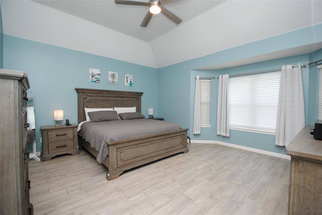 Spacious living room with vaulted ceilings, fits a large sectional sofa, hardwood floors, and a cozy fireplace. Ample natural light from large windows complements the modern decor, with a ceiling fan for added comfort.