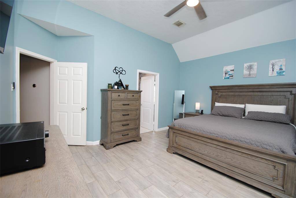 This spacious bedroom features a calming blue color scheme, large windows with white curtains allowing ample natural light, and a ceiling fan.
