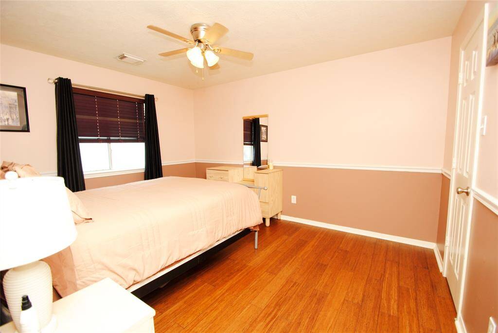This spacious room features hardwood floors and a high ceiling with a ceiling fan, complemented by built-in bookshelves. A large window allows natural light to fill the space.