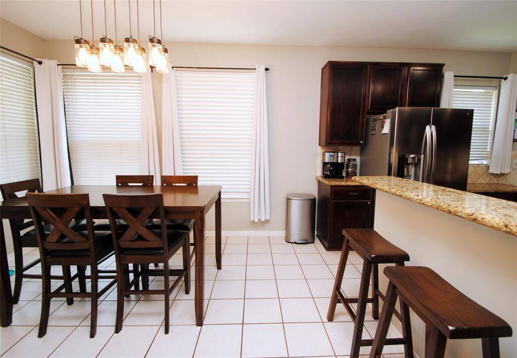 This spacious kitchen features granite countertops, dark wood cabinets, stainless steel appliances, and a central island. It has ample natural light and a modern, open layout.